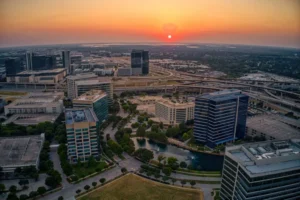 Aerial view of a city skyline at sunset with office towers, highways and green space