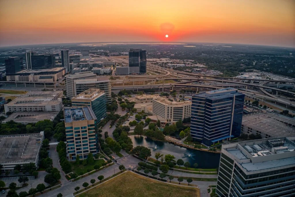 Aerial view of a city skyline at sunset with office towers, highways and green space