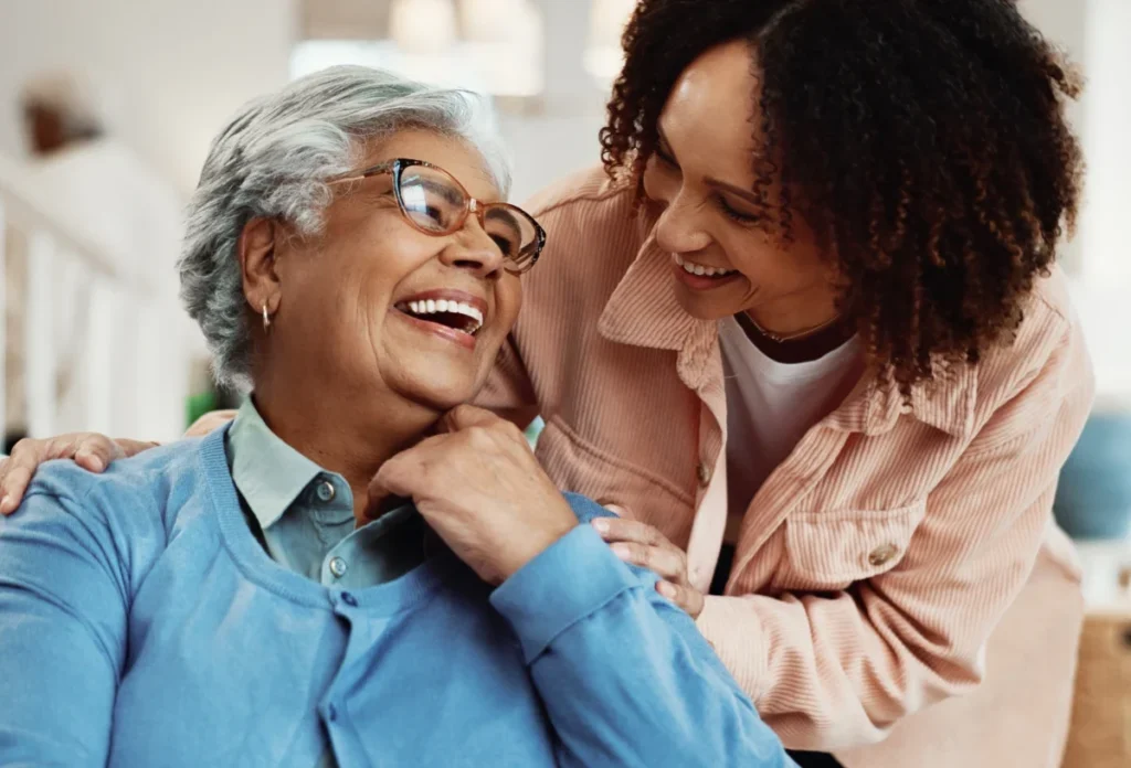 Older woman in glasses laughing while a younger woman leans in beside her