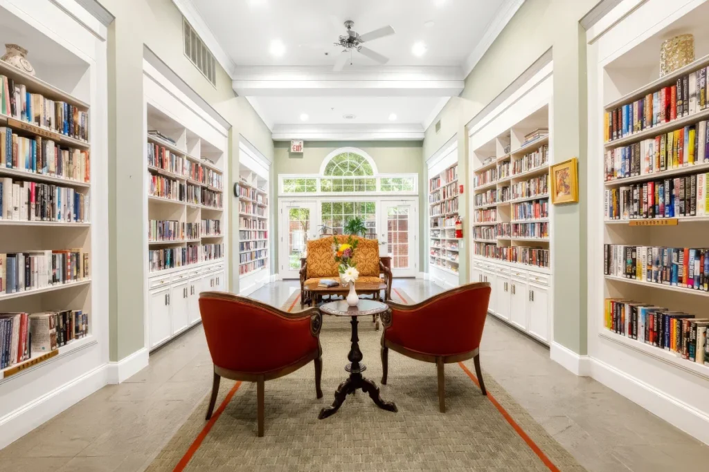 Library hallway lined with built-in bookshelves full of books, with two red chairs and a small table at the end