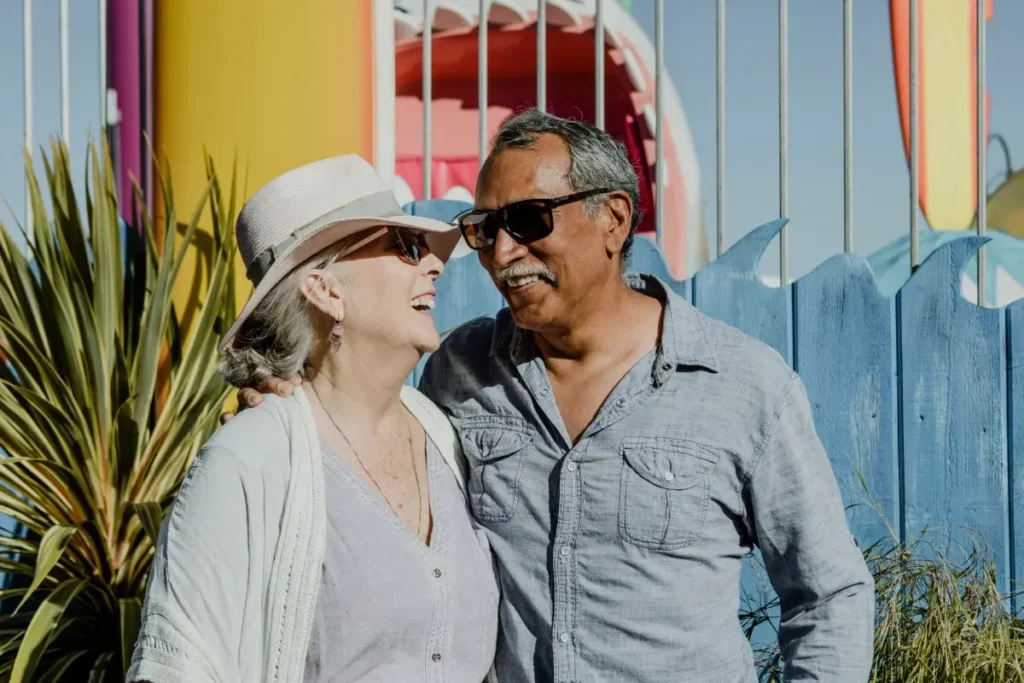 Smiling older couple in a sun hat and sunglasses standing together in front of colorful buildings